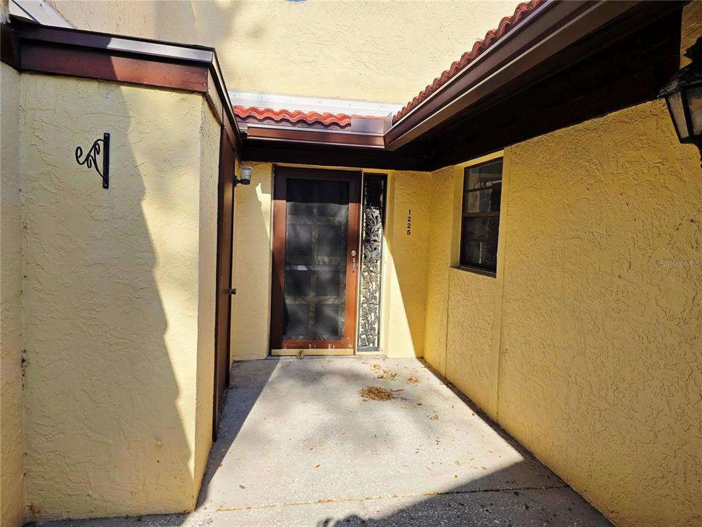 A yellow stucco house exterior features a front door with a screen and side window — 1225 56TH STREET W, BRADENTON, FL