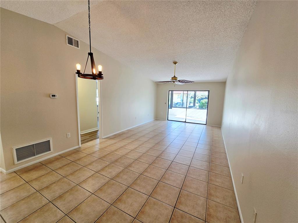 An empty room features beige tile flooring, a ceiling fan, and a hanging light fixture — 1225 56TH STREET W, BRADENTON, FL