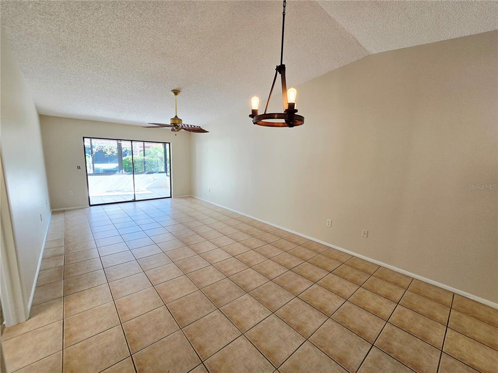 An empty dining area features tile flooring, a rustic chandelier, and a sliding glass door — 1225 56TH STREET W, BRADENTON, FL