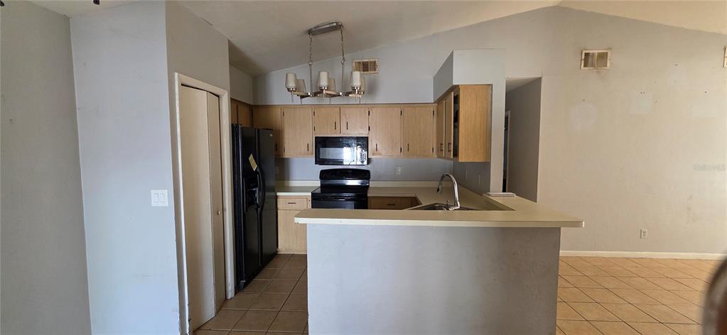 A kitchen features light wood cabinets, black appliances, a breakfast bar, and tile flooring — 721 NE 26TH STREET, OCALA, FL