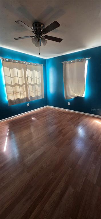 A bedroom with blue walls, wood-look flooring, a ceiling fan, and two windows with curtains — 721 NE 26TH STREET, OCALA, FL