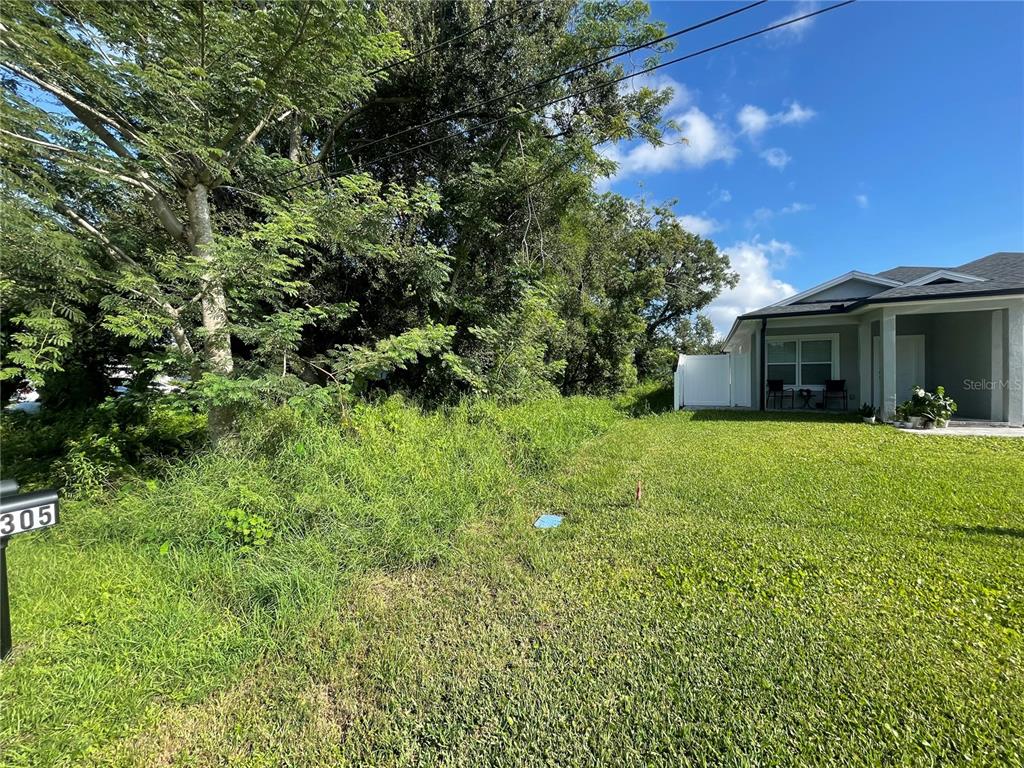 A grassy lot with overgrown vegetation sits next to a modern single-story house — 305 CYPRESS STREET, ORLANDO, FL