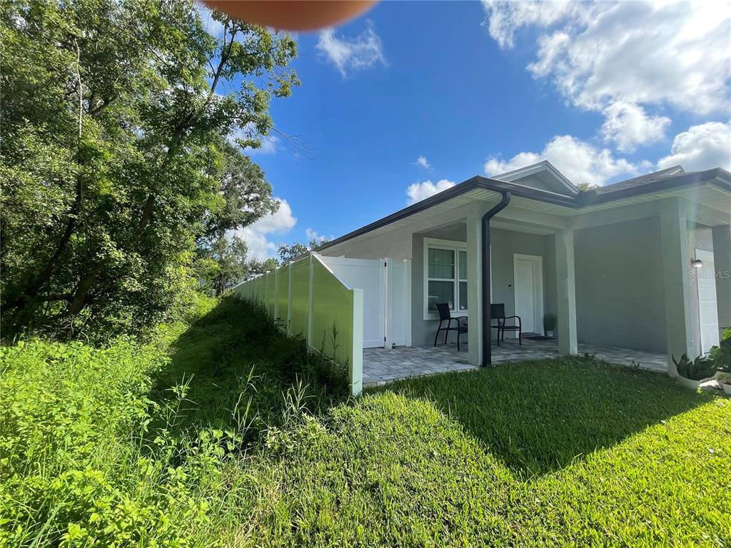 A side view of a house exterior featuring a paved patio and a white privacy fence — 305 CYPRESS STREET, ORLANDO, FL