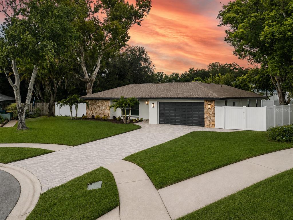 A single-story house with a stone facade, dark garage door, and paved driveway at sunset — 1967 CASTILLE DRIVE, DUNEDIN, FL
