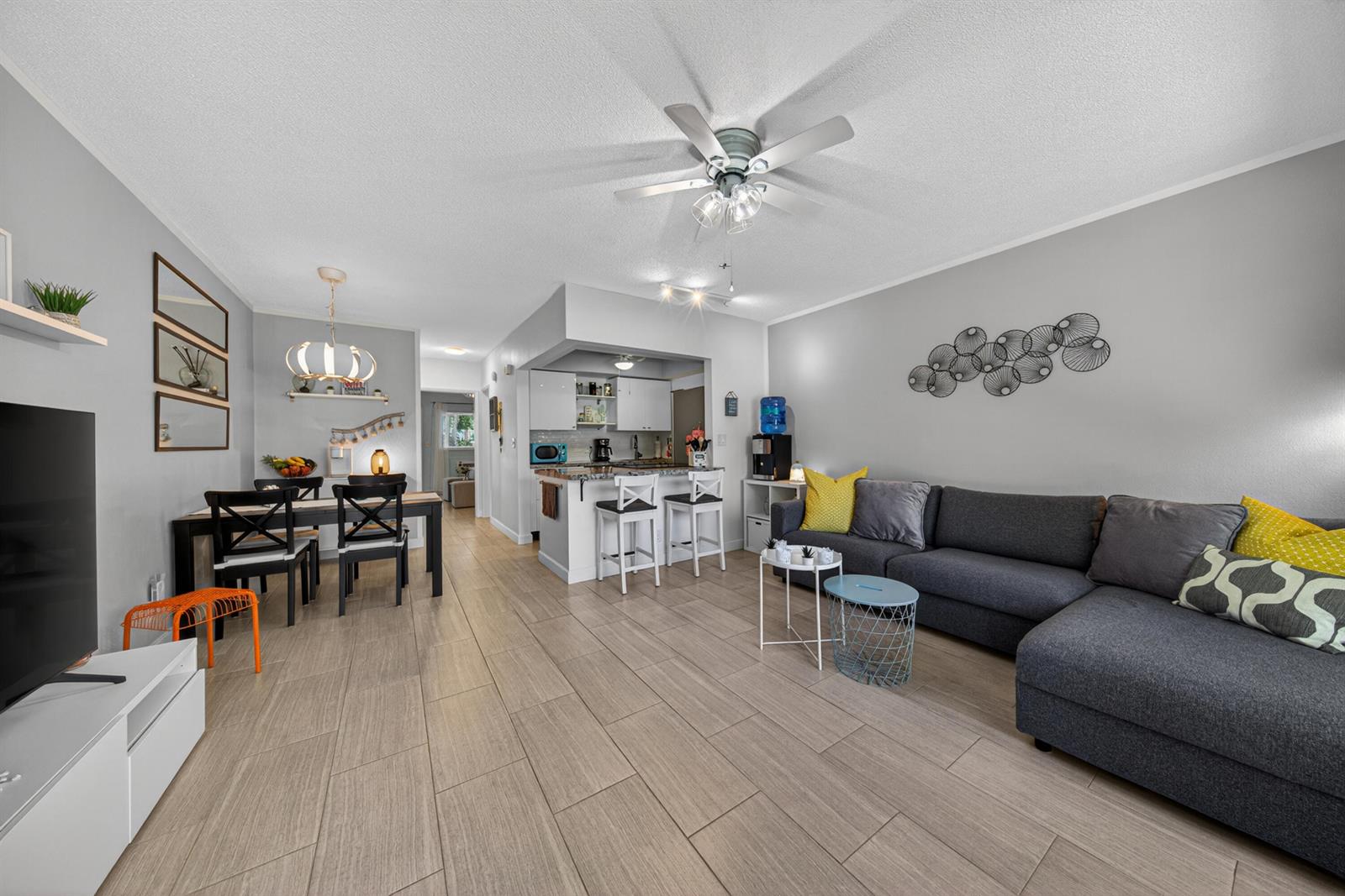 An open-concept living and dining area features gray tile flooring, a sectional sofa, and kitchen — 3201 SE 10th Street # A11, Pompano Beach FL 33062, POMPANO BEACH, FL