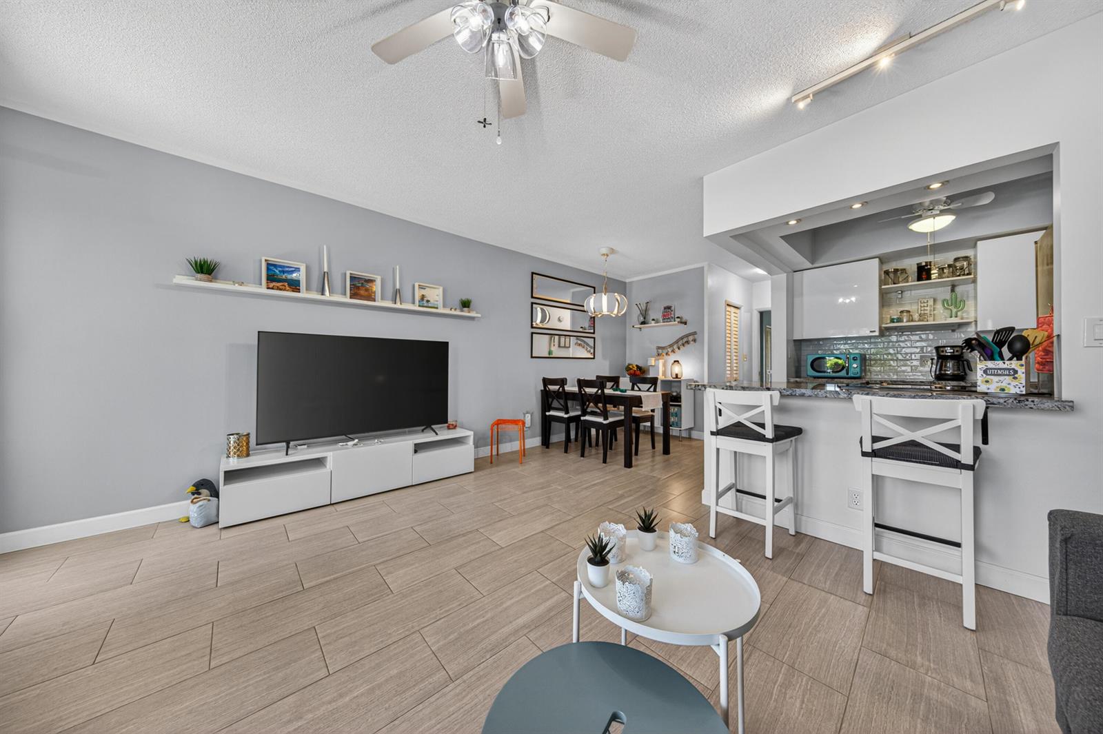 An open-concept living and dining area features light tile flooring, a white media console, and kitchen bar seating — 3201 SE 10th Street # A11, Pompano Beach FL 33062, POMPANO BEACH, FL
