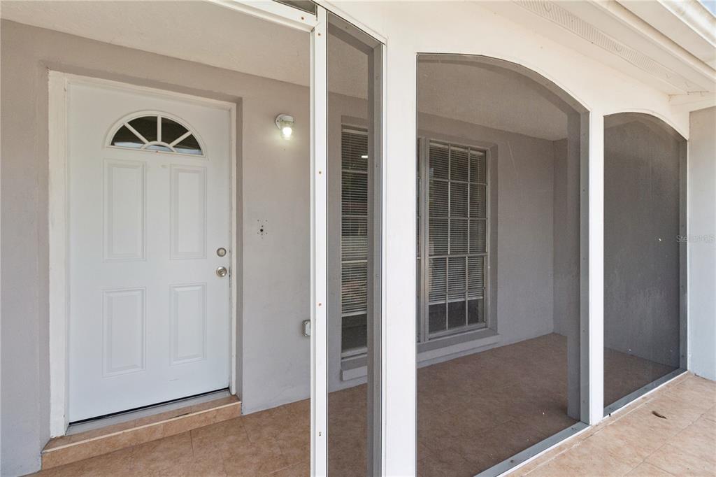 A white front door opens onto a tiled porch enclosed by a screened-in frame — 6835 MESA VERDE STREET, PORT RICHEY, FL