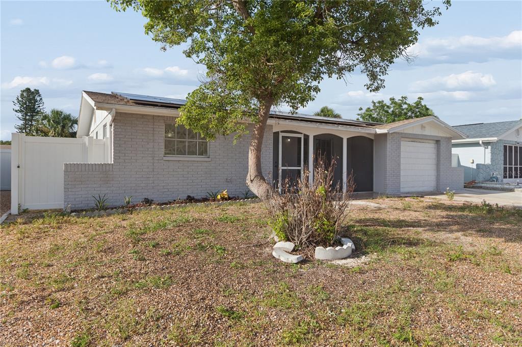 A single-story brick house with a white garage, a large tree, and a white fence — 6835 MESA VERDE STREET, PORT RICHEY, FL