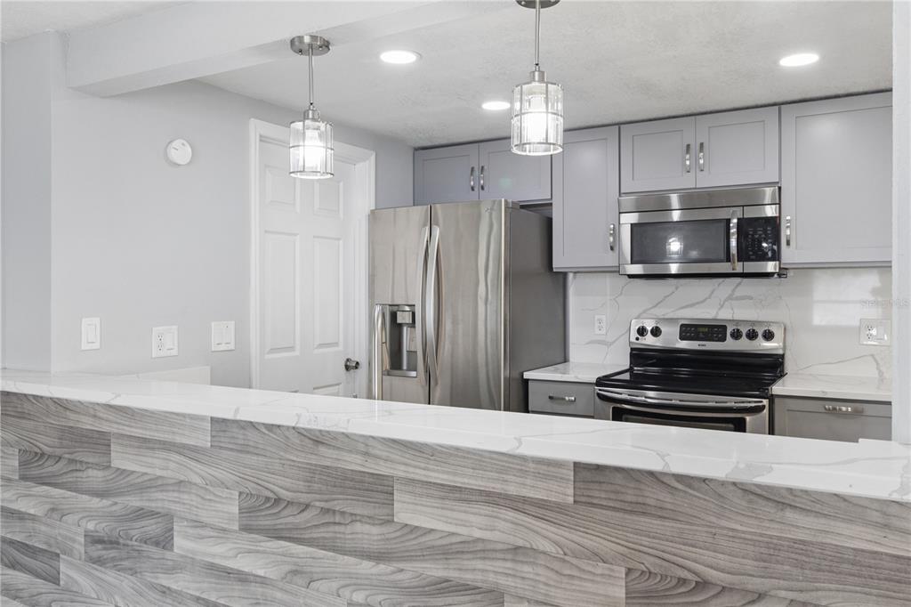 A kitchen features gray cabinets, stainless steel appliances, and a wood-paneled breakfast bar with countertops — 6835 MESA VERDE STREET, PORT RICHEY, FL