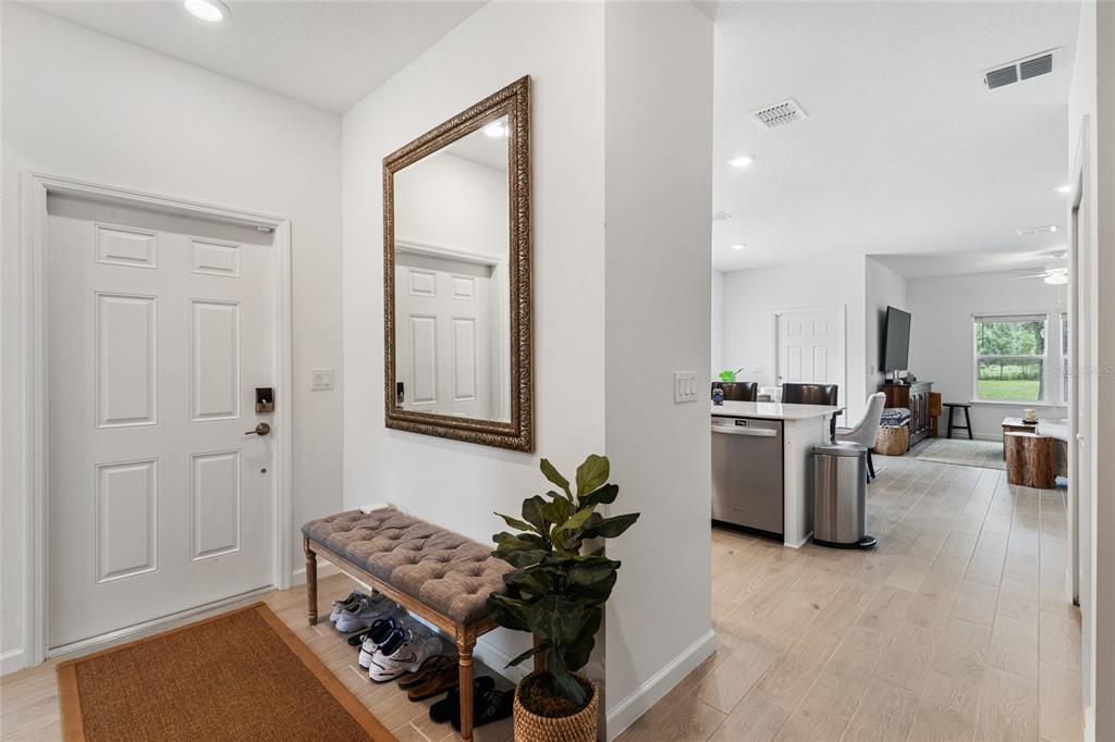 A foyer with a tufted bench and mirror leads into an open-concept kitchen and living area — 692 NW 126TH TERRACE UNIT 692, NEWBERRY, FL