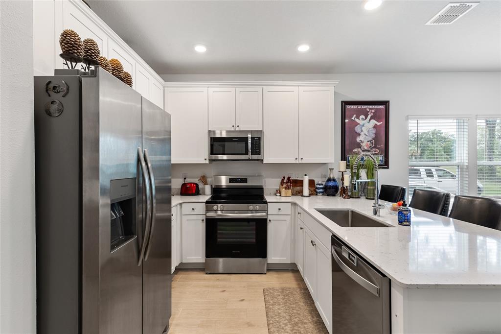 A kitchen features white cabinets, stainless steel appliances, a quartz island, and light wood flooring — 692 NW 126TH TERRACE UNIT 692, NEWBERRY, FL