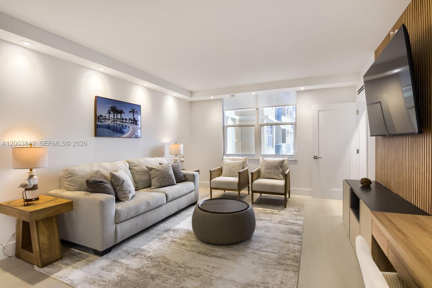 A living room features a beige sofa, two armchairs, a round ottoman, and a wall-mounted television — 2501 S Ocean Dr # 833, Hollywood FL 33019, HOLLYWOOD, FL