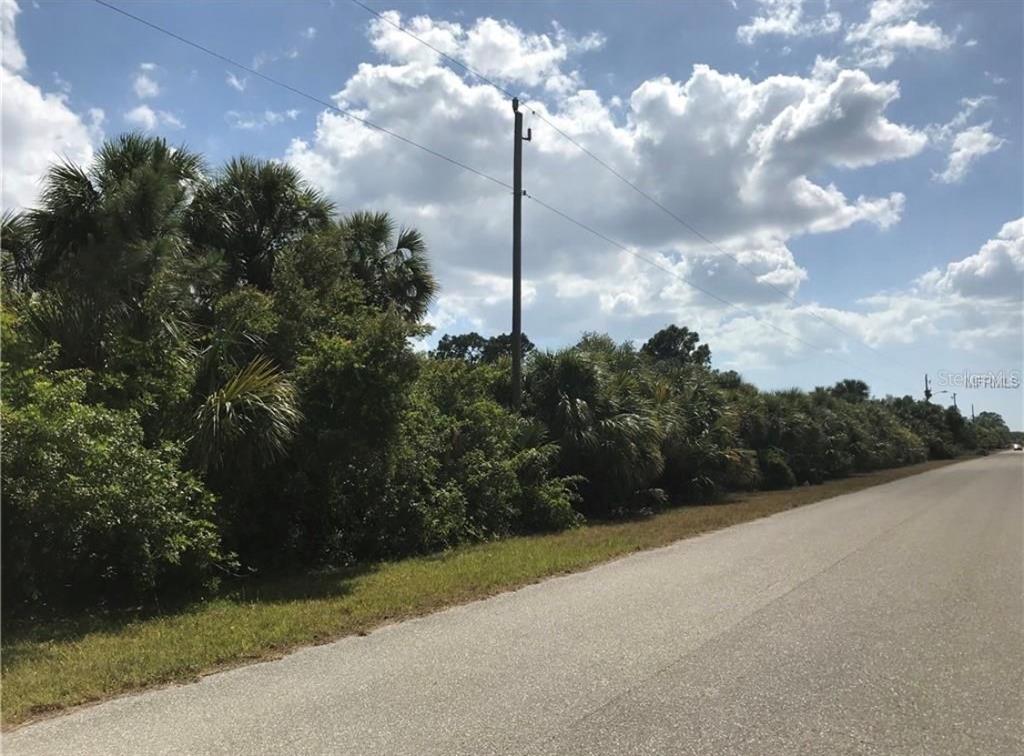 A paved road runs alongside a dense line of trees and shrubs under a cloudy sky — 14227 PITTENGER AVENUE, PORT CHARLOTTE, FL