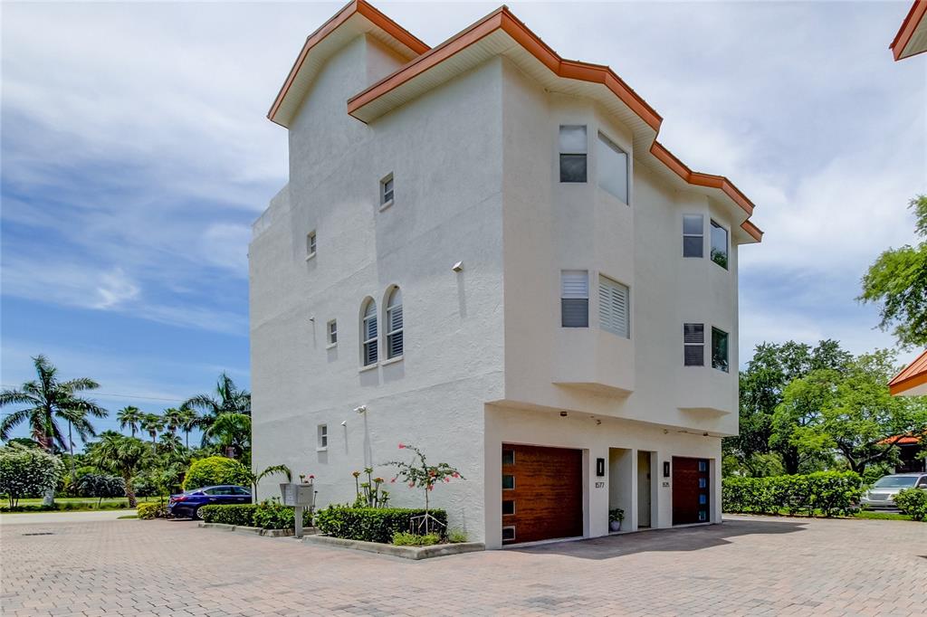 A three-story white stucco townhouse with a paved driveway and two wooden garage doors — 1575 PINELLAS BAYWAY WAY S UNIT 1575, TIERRA VERDE, FL