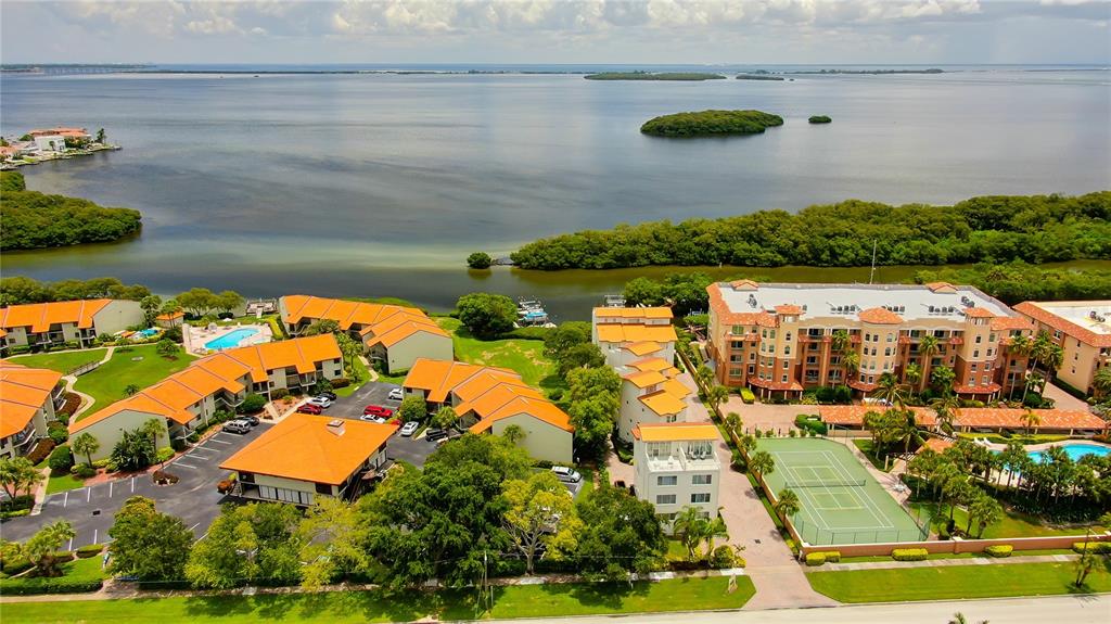An aerial view shows a waterfront residential complex with orange-roofed buildings and a tennis court — 1575 PINELLAS BAYWAY WAY S UNIT 1575, TIERRA VERDE, FL