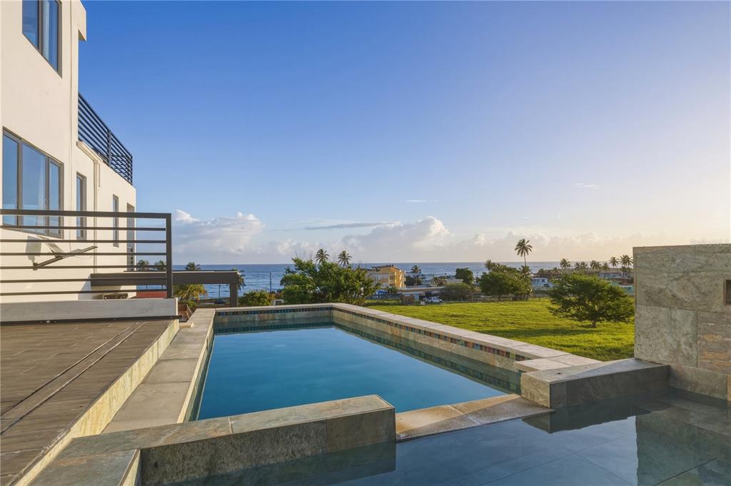 A modern infinity pool overlooks a grassy field and the ocean from a balcony — Bo. Membrillo Solar 1, CAMUY, PR