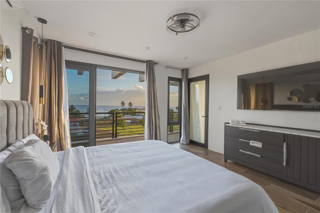 A bedroom features a bed, a wall-mounted television, and a balcony overlooking the ocean — Bo. Membrillo Solar 1, CAMUY, PR