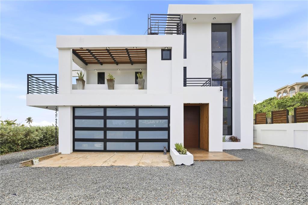 A modern two-story white house with a glass garage door and a wooden pergola balcony — Bo. Membrillo Solar 1, CAMUY, PR