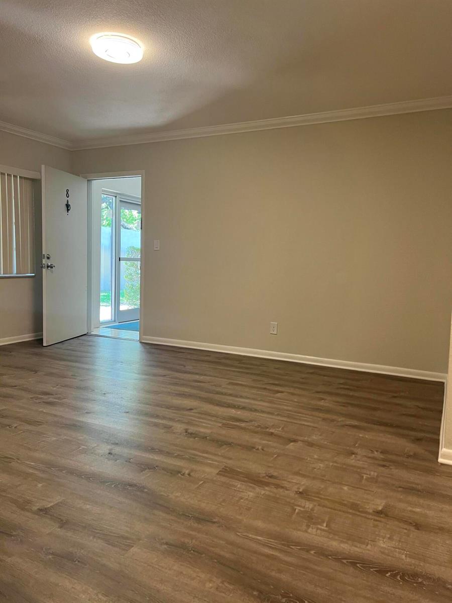 An empty room features light-colored walls, wood-look flooring, and a door leading to a patio — 3550 NW 8th Avenue # 808, Pompano Beach FL 33064, POMPANO BEACH, FL