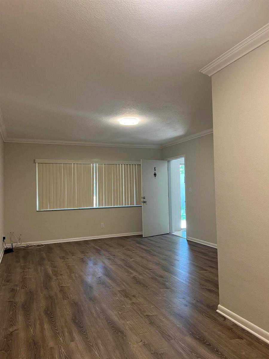 An empty room with wood-look flooring, beige walls, a window with blinds, and an open door — 3550 NW 8th Avenue # 808, Pompano Beach FL 33064, POMPANO BEACH, FL