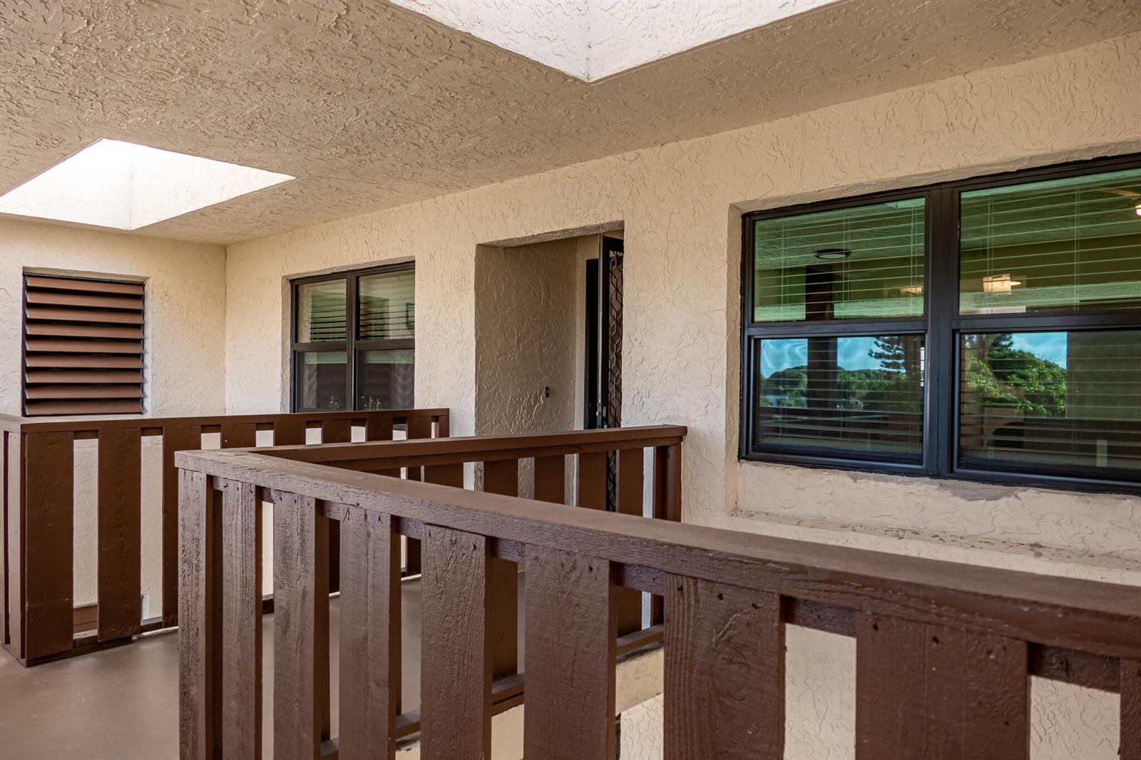 An outdoor balcony with brown wooden railings and stucco walls features two windows and a doorway — 162 SE Saint Lucie Boulevard # B403, Stuart FL 34996, STUART, FL