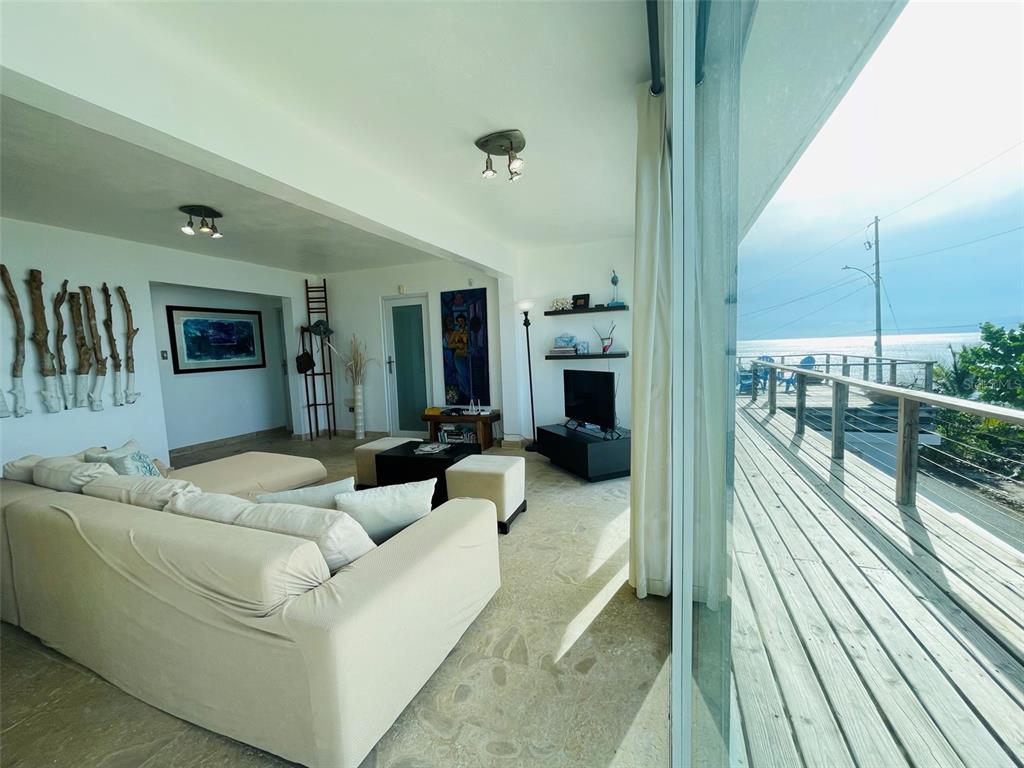 A living room with a beige sofa opens onto a wooden deck overlooking the ocean — 56 N SHORE ROAD, VIEQUES, PR