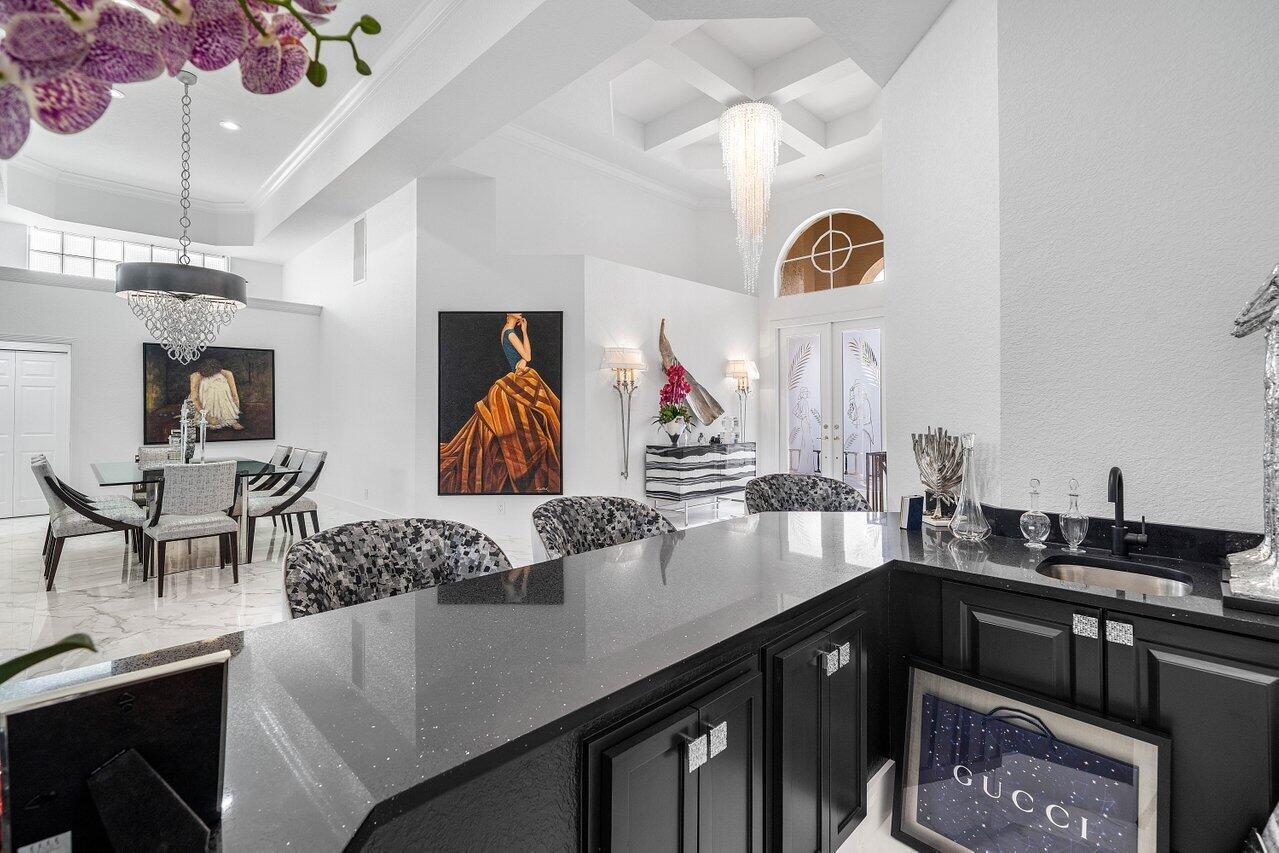 A modern kitchen with black cabinetry and countertops overlooks a dining area with chandeliers — 6517 Somerset Circle, Boca Raton FL 33496, BOCA RATON, FL