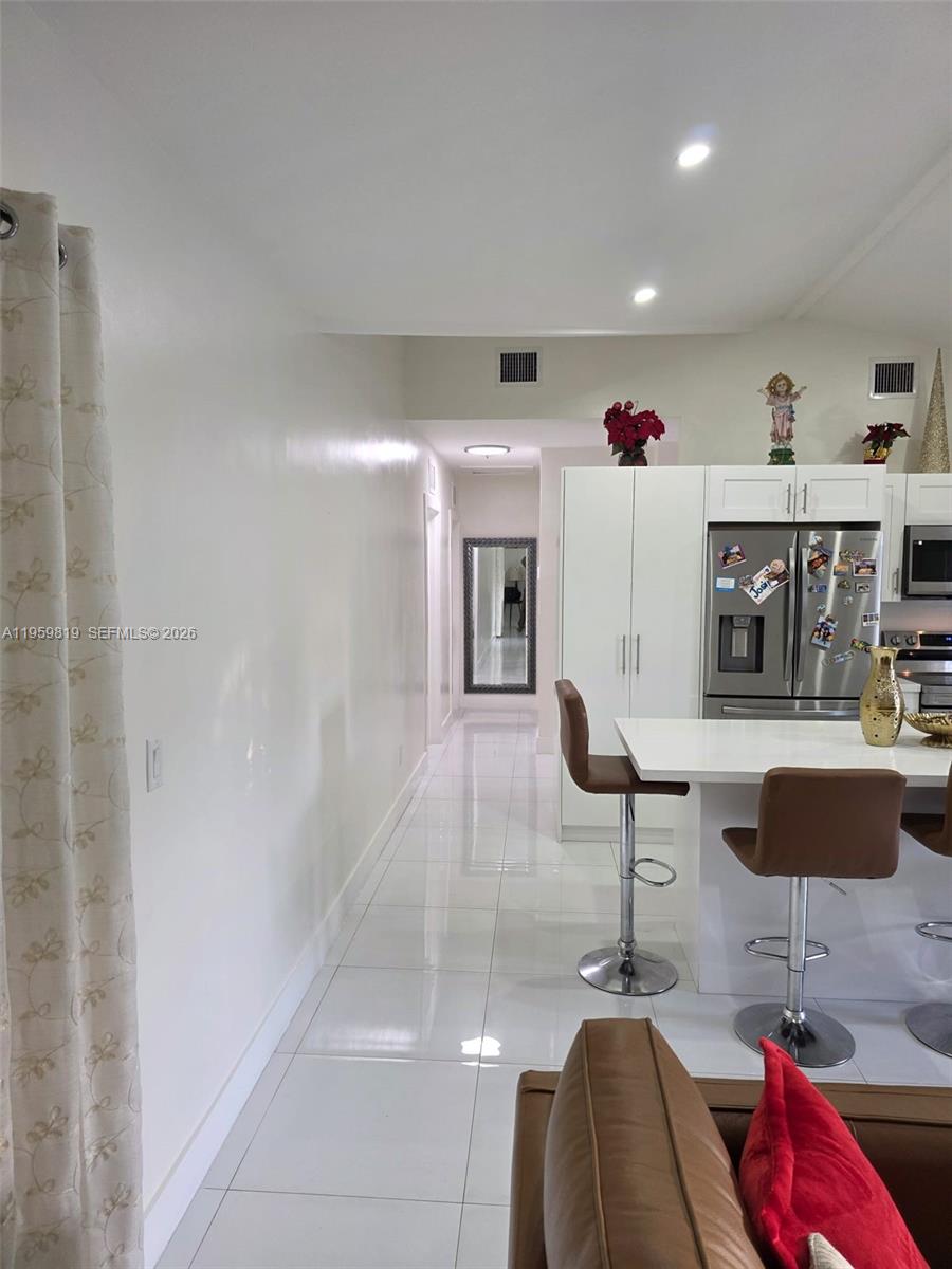 A kitchen with white cabinets and a breakfast bar overlooks a hallway with tile floors — 8523 NW 35th Pl, Miami FL 33147, MIAMI, FL