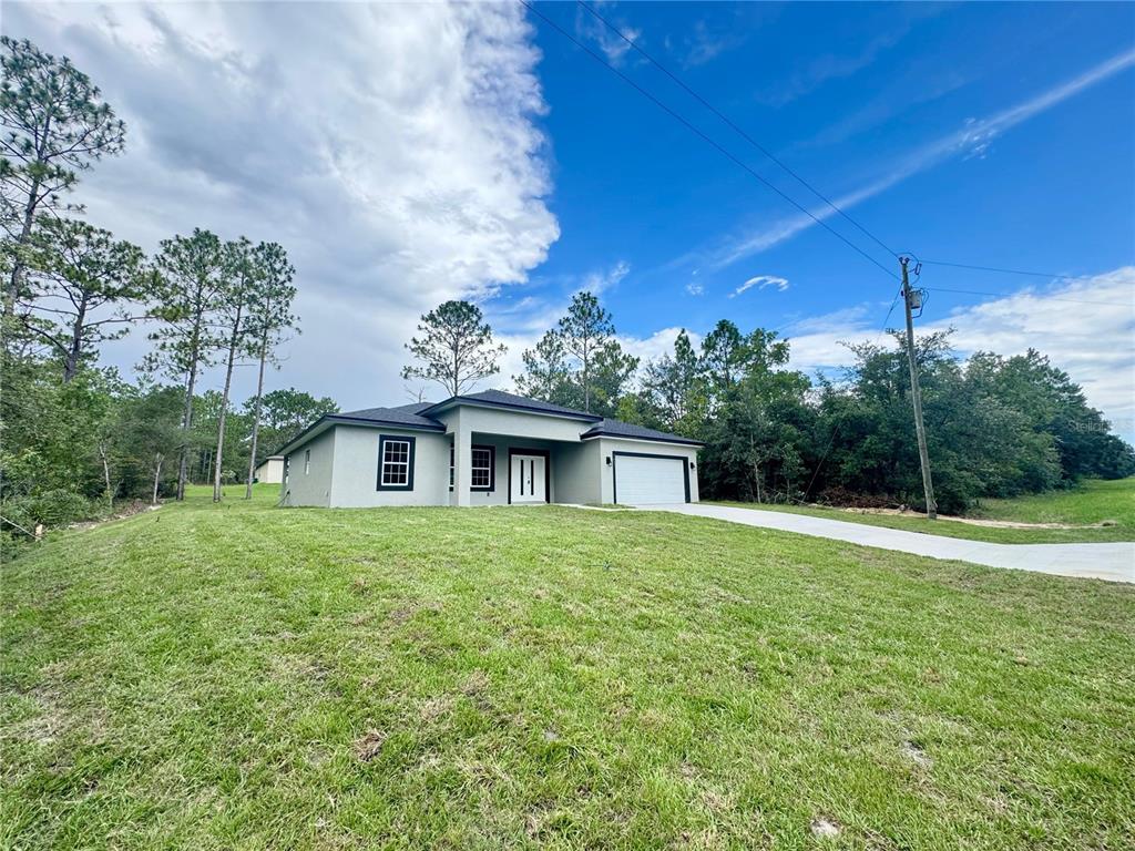 A single-story house with a white garage and a grassy yard under a blue sky — 7035 N MALTESE DRIVE, CITRUS SPRINGS, FL