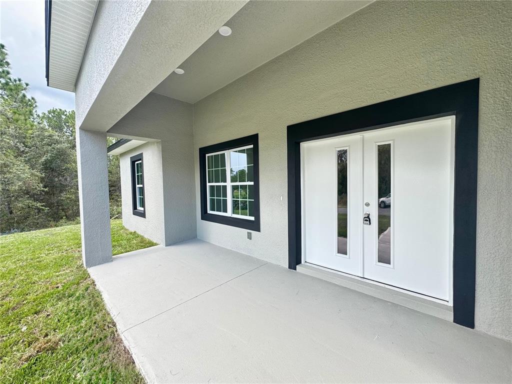 A covered concrete porch features a double front door and windows with black trim — 7035 N MALTESE DRIVE, CITRUS SPRINGS, FL