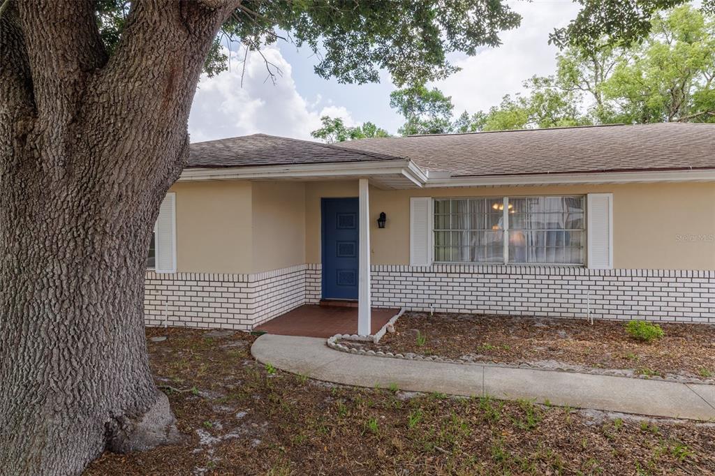 A single-story house exterior features a blue front door, white brick base, and large tree — 1987 S OLD MILL DRIVE, DELTONA, FL