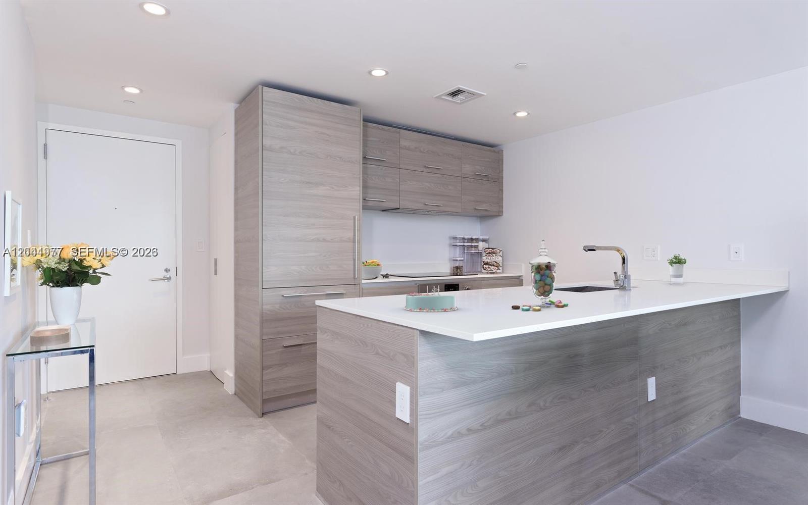 A modern kitchen features light wood-grain cabinetry, a white quartz island, and gray tile flooring — 1300 S Miami Ave # 3311, Miami FL 33130, MIAMI, FL