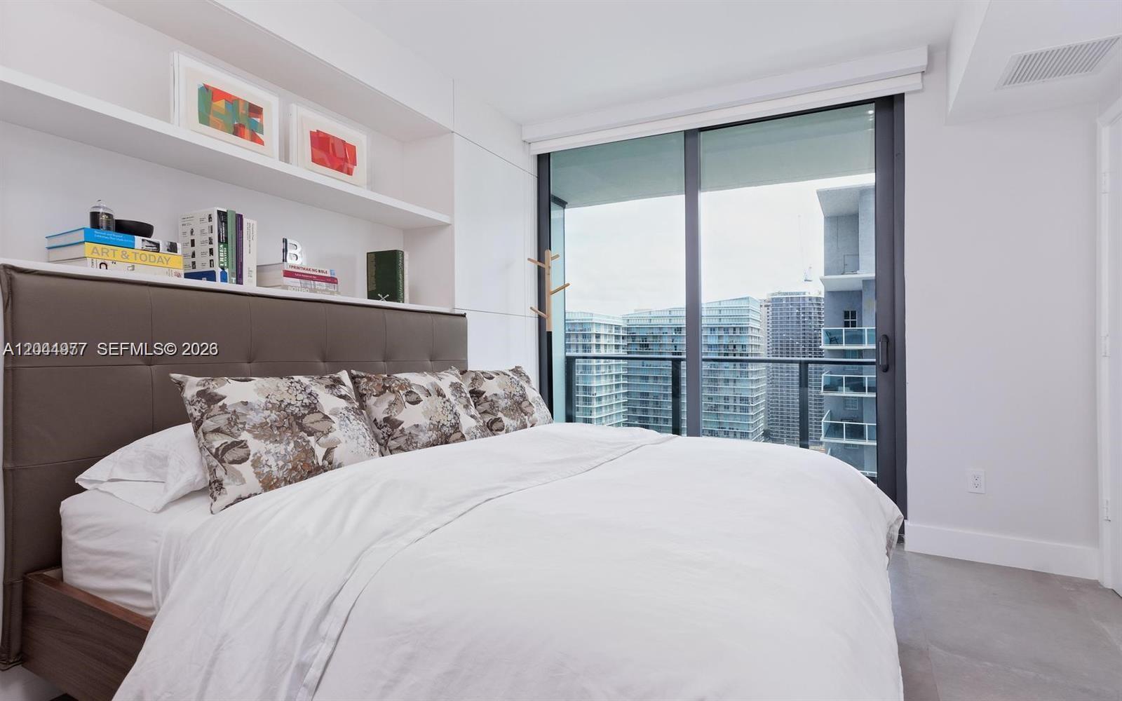 A modern bedroom features a bed with floral pillows, built-in shelving, and floor-to-ceiling windows — 1300 S Miami Ave # 3311, Miami FL 33130, MIAMI, FL