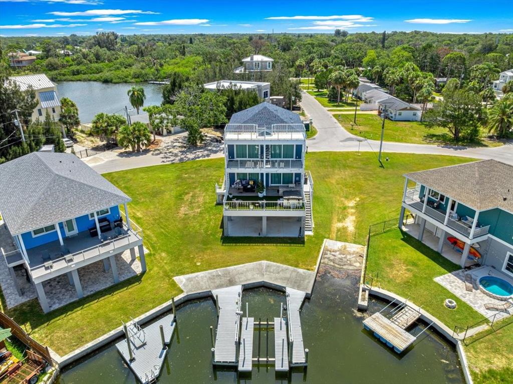 An aerial view shows three elevated waterfront houses with private docks along a canal — 6812 DRIFTWOOD DRIVE, HUDSON, FL
