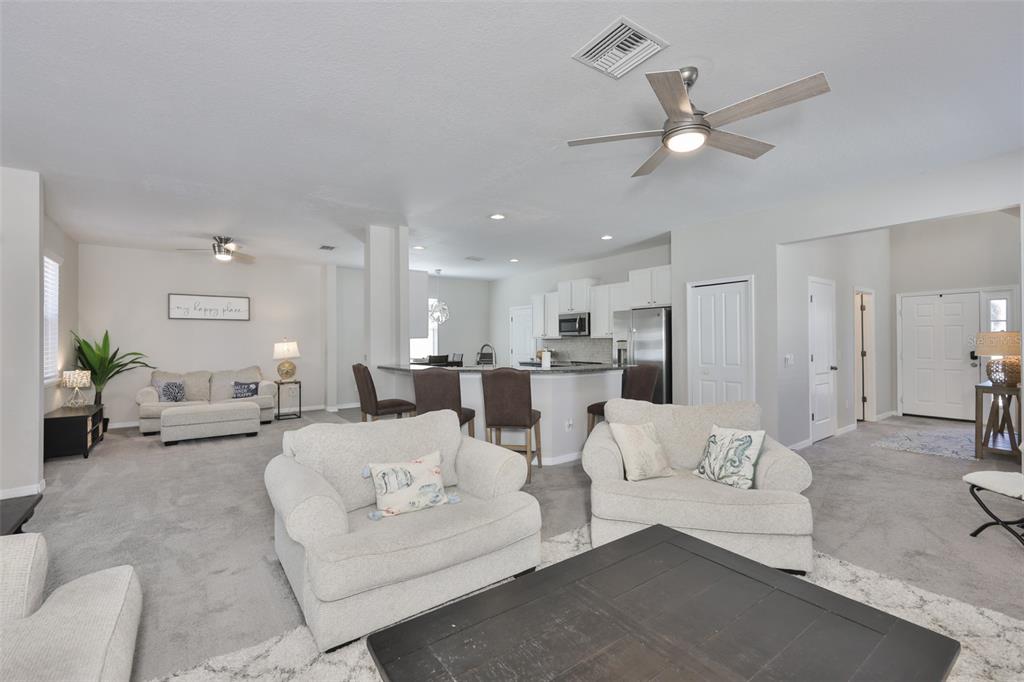 A spacious open-concept living room features light-colored carpet, neutral walls, and a kitchen island — 1609 BONITA BLUFF COURT, RUSKIN, FL