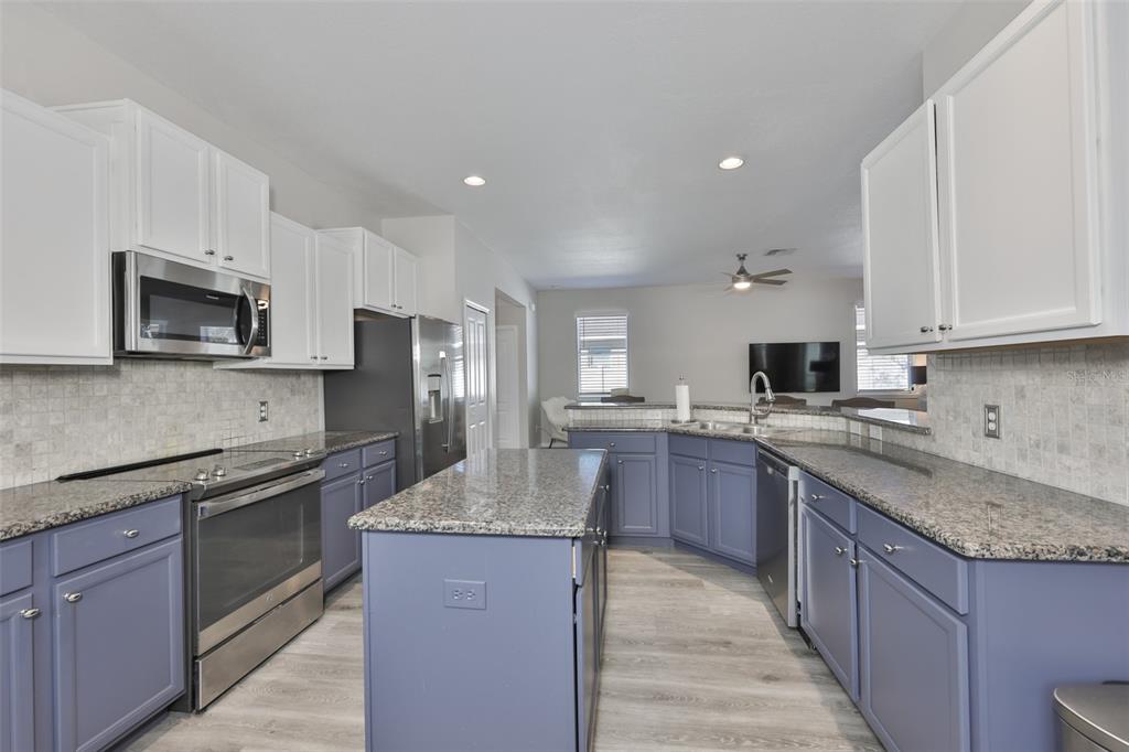 A kitchen features blue lower cabinets, white upper cabinets, granite countertops, and stainless steel appliances — 1609 BONITA BLUFF COURT, RUSKIN, FL