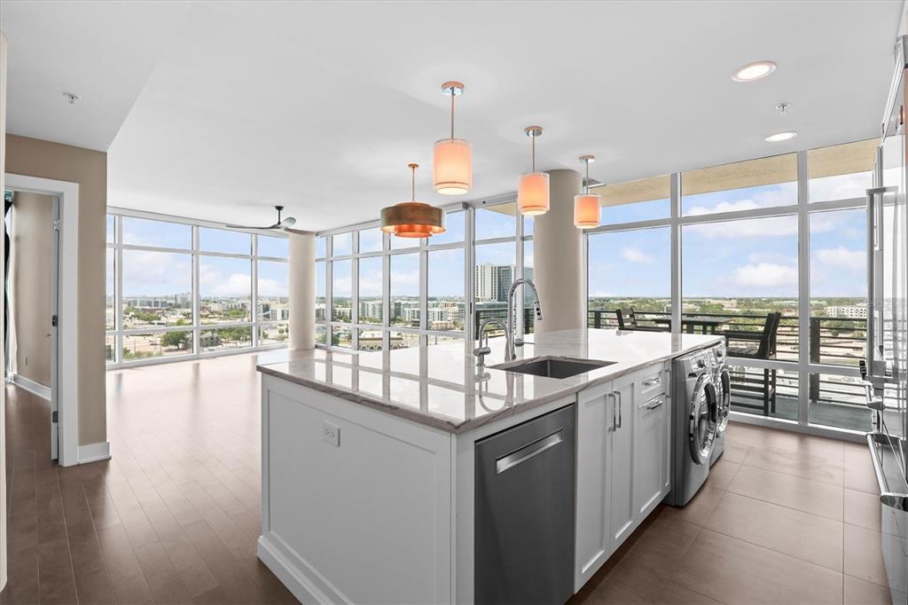 A modern kitchen island with a sink and built-in laundry appliances sits before floor-to-ceiling windows — 1120 E KENNEDY BOULEVARD UNIT 1216, TAMPA, FL