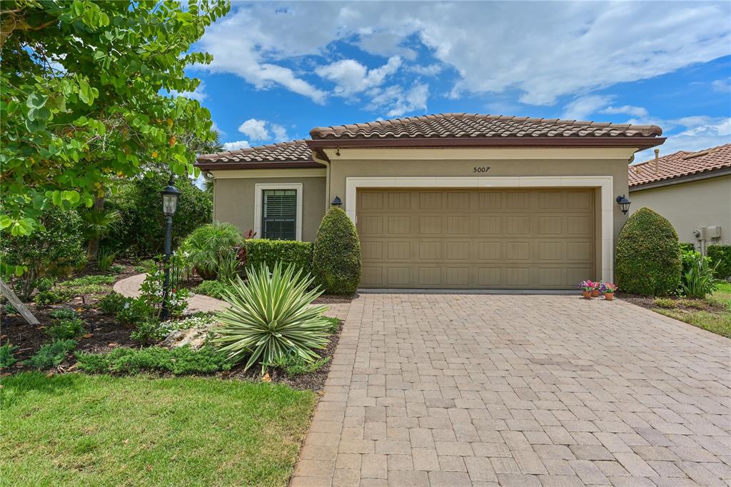 A single-story house with a tan stucco exterior, a tile roof, and a paved driveway — 5007 SERATA DRIVE, BRADENTON, FL