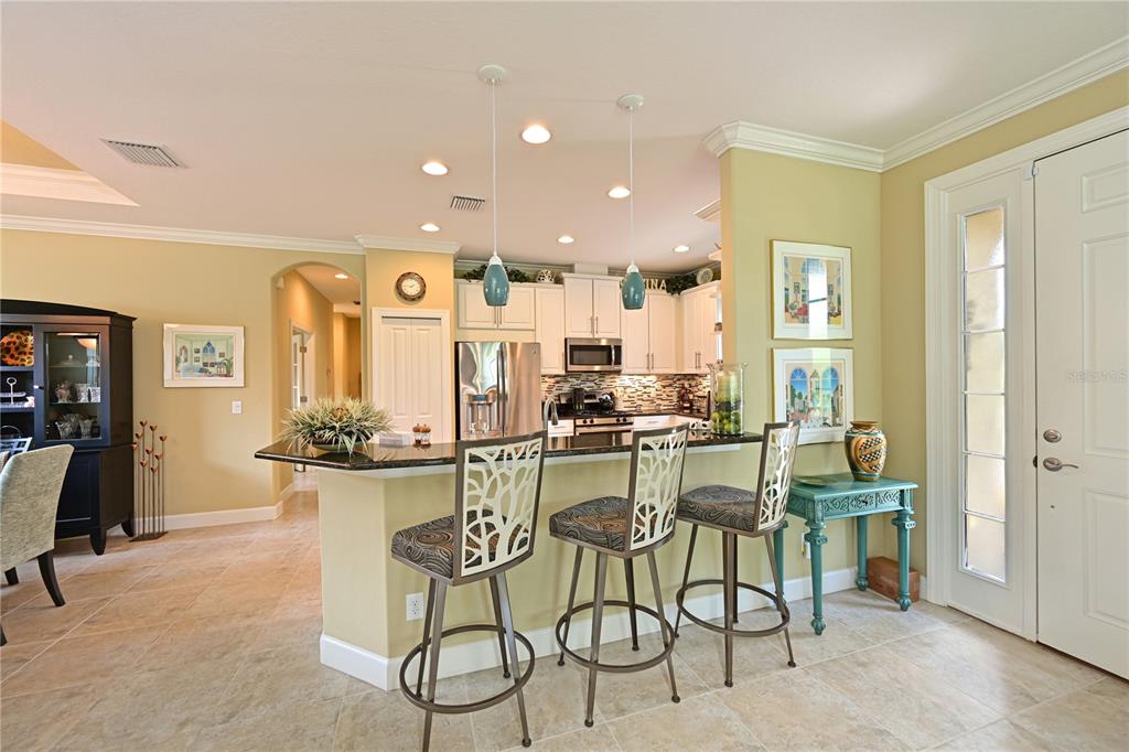 A kitchen with white cabinets, a granite breakfast bar, and three stools on tile flooring — 5007 SERATA DRIVE, BRADENTON, FL