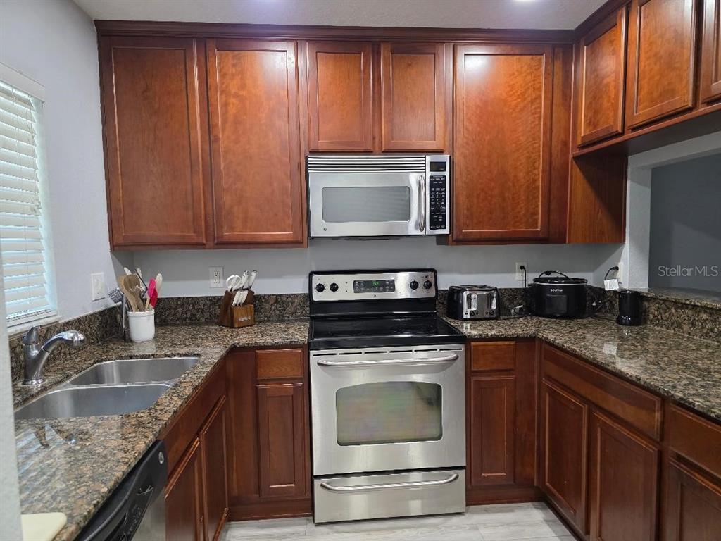 A kitchen features dark wood cabinets, granite countertops, and stainless steel appliances — 37613 AARALYN ROAD, ZEPHYRHILLS, FL