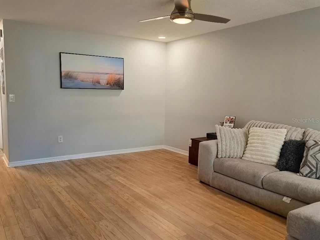 A living room features light wood-look flooring, gray walls, a ceiling fan, and a sofa — 37613 AARALYN ROAD, ZEPHYRHILLS, FL
