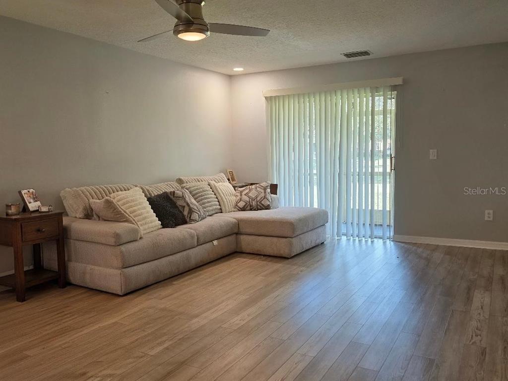 A living room features light wood-look flooring, a large sectional sofa, and sliding glass doors — 37613 AARALYN ROAD, ZEPHYRHILLS, FL