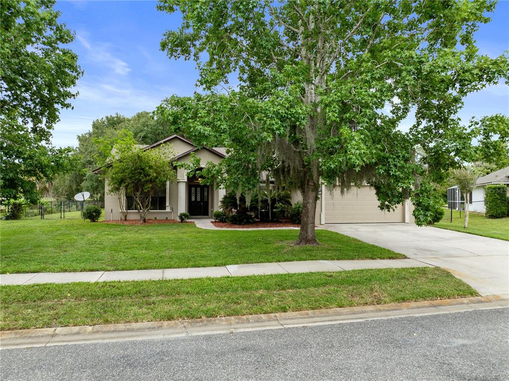 A single-story house with a beige exterior, a two-car garage, and a large front tree — 4924 RAYLENE WAY, ST CLOUD, FL