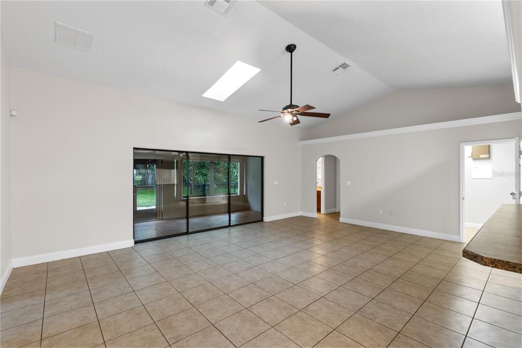 A spacious living room features vaulted ceilings, tile flooring, a ceiling fan, and sliding glass doors — 4924 RAYLENE WAY, ST CLOUD, FL