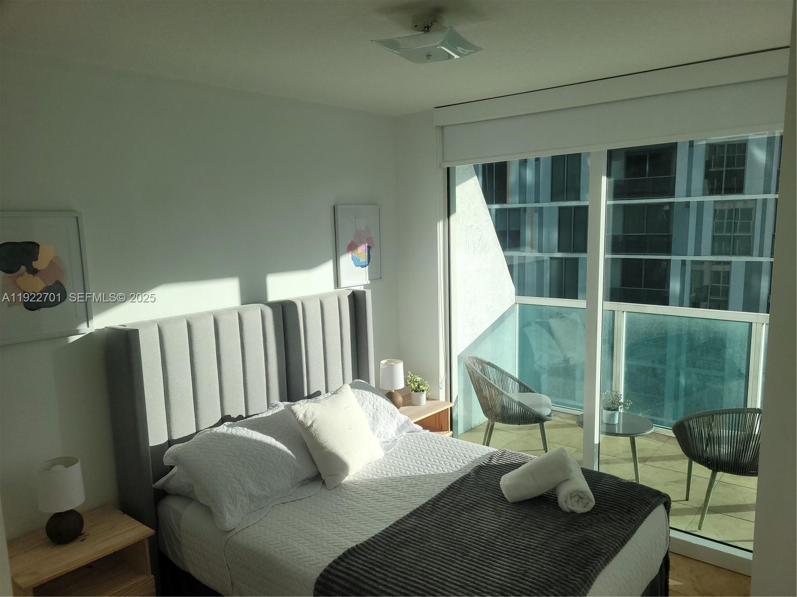 A bedroom with a gray upholstered headboard, white bedding, and a balcony with outdoor seating — 41 SE 5th St # 710, Miami FL 33131, MIAMI, FL