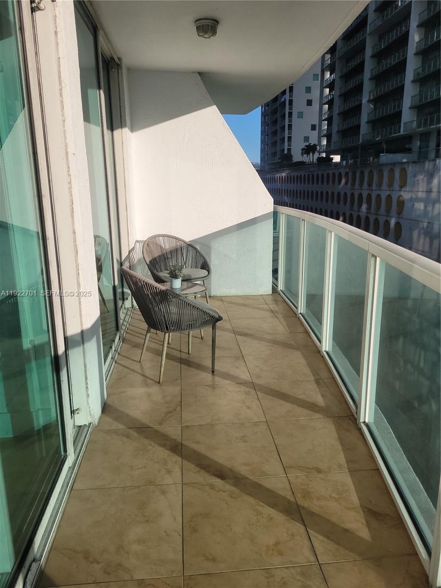 A balcony with tiled flooring, two chairs, and a glass railing overlooking a city building — 41 SE 5th St # 710, Miami FL 33131, MIAMI, FL