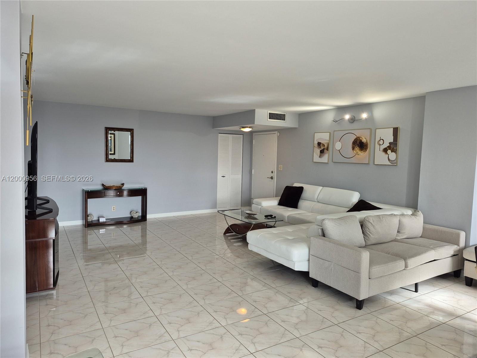 A living room features light gray walls, tile flooring, a white sectional, and a beige sofa — 1912 S Ocean Dr # 17C, Hallandale Beach FL 33009, HALLANDALE BEACH, FL