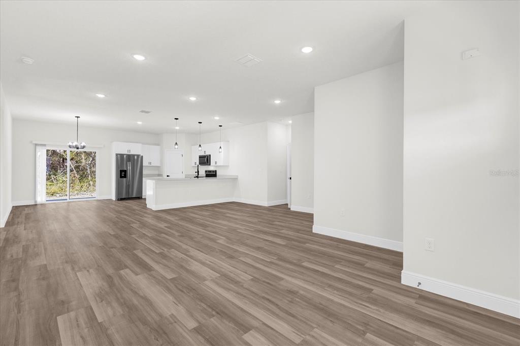 An open-concept kitchen and living area features white cabinetry, stainless steel appliances, and wood-look flooring — 13592 SW 40 CIRCLE, OCALA, FL