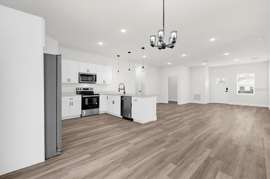 A modern kitchen with white cabinets and a center island opens into a spacious living area — 13592 SW 40 CIRCLE, OCALA, FL