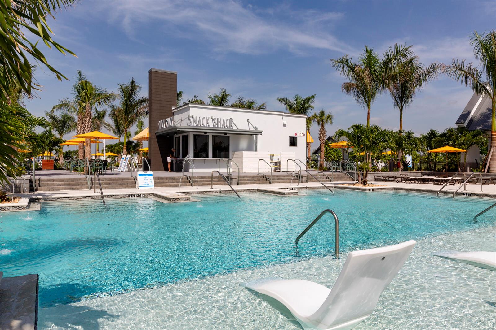 A swimming pool with lounge chairs sits in front of a white snack shack building — 14141 Spruce Pine Drive, Westlake FL 33470, WESTLAKE, FL